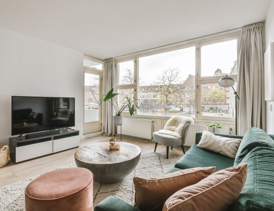 Lichte woonkamer met groene bank en grote ramen in een woning met energielabel in Voorschoten